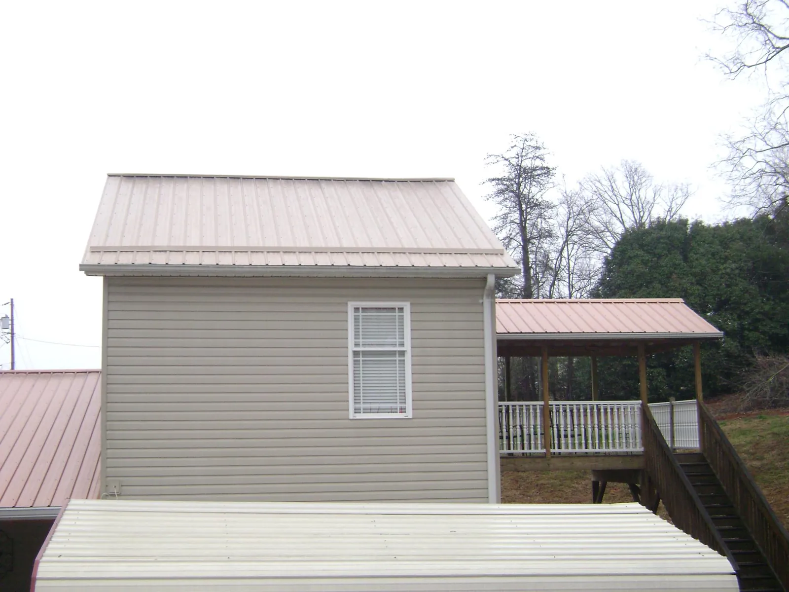 Tan metal roofs on a two story addition and attached porch, from a Roof Replacement job in Coventry